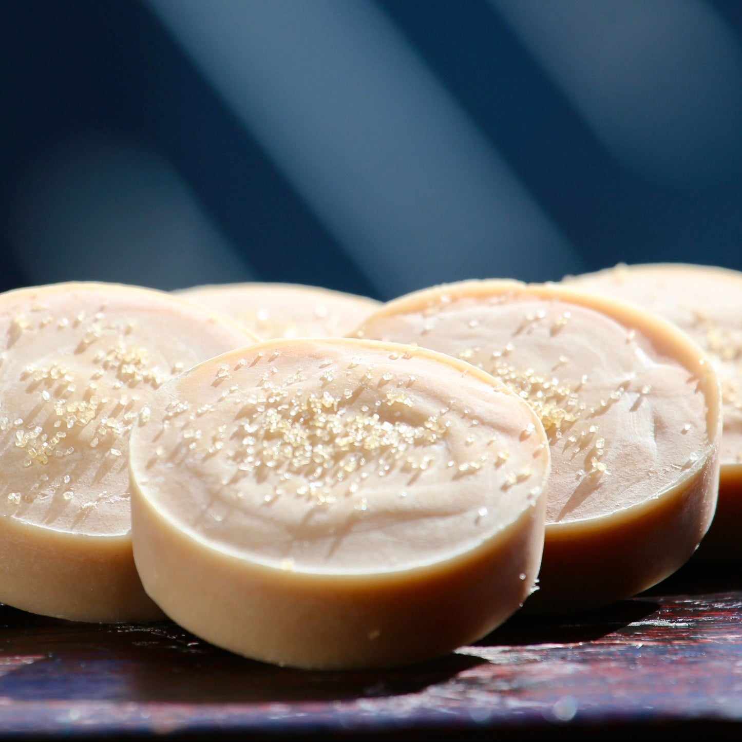 Sliced white bar of soap with sugar on top on a dark surface with a blurred blue background