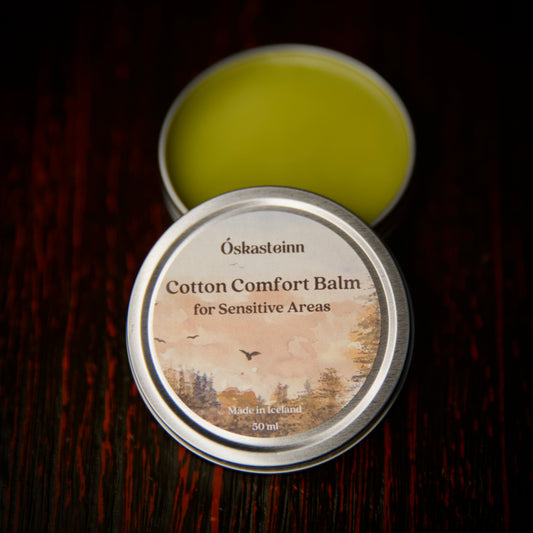 Cotton Comfort Balm container with lid open on a dark wooden surface