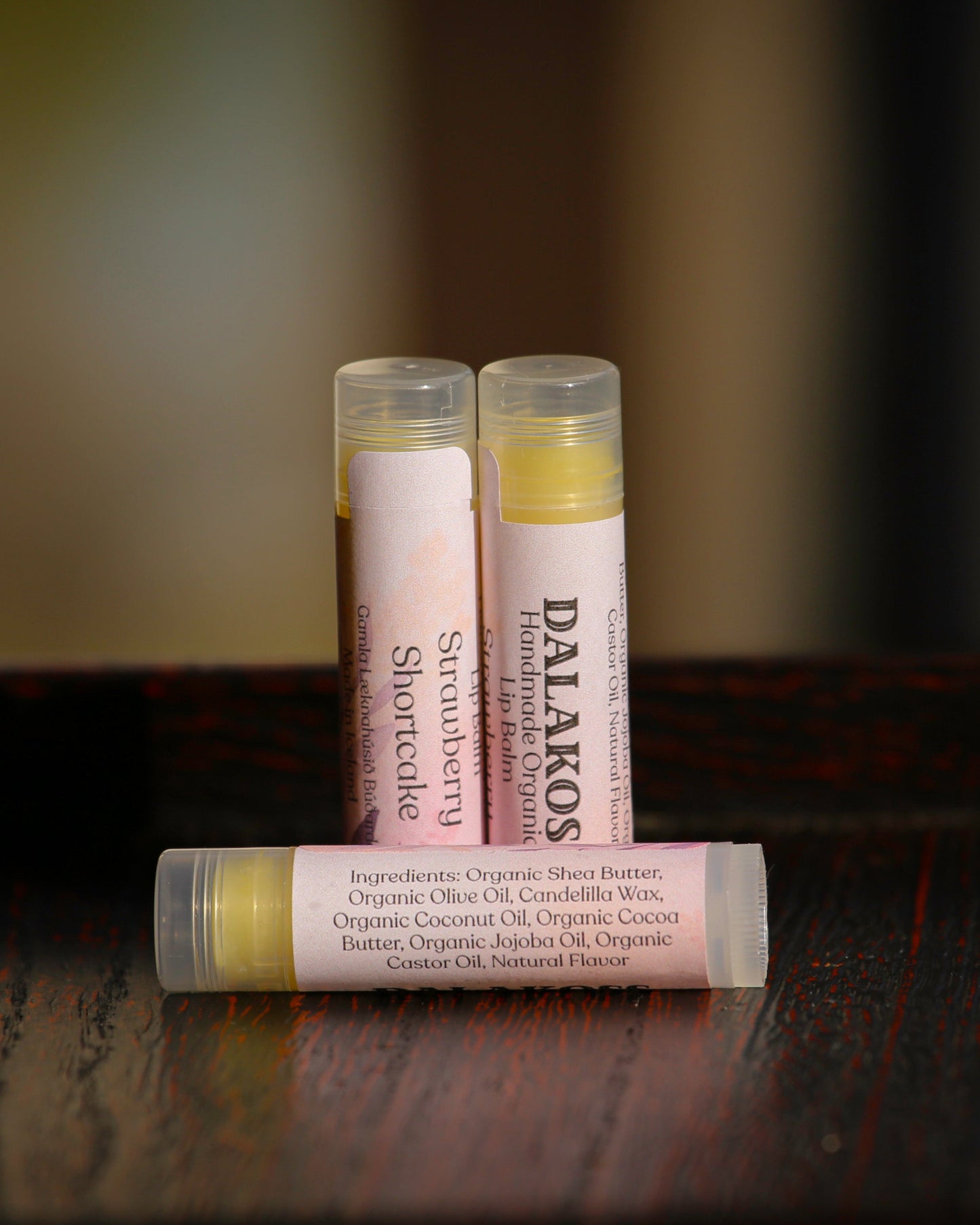 Three lip balm tubes with visible Dalakoss branding on a wooden surface.