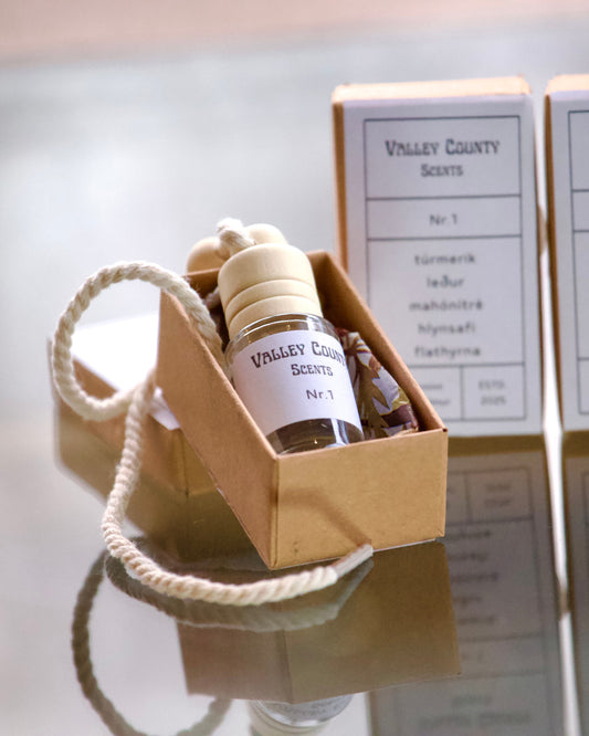 Small car diffuser bottle with a rope and boxes labeled 'Valley County Scents' on a reflective surface.