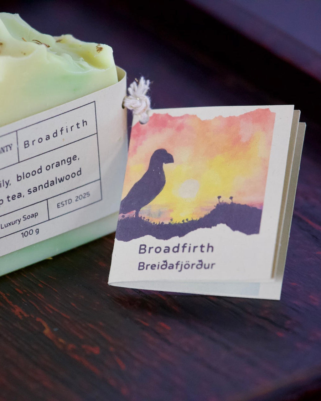 Two bars of soap with packaging featuring a scenic illustration and text on a dark surface.