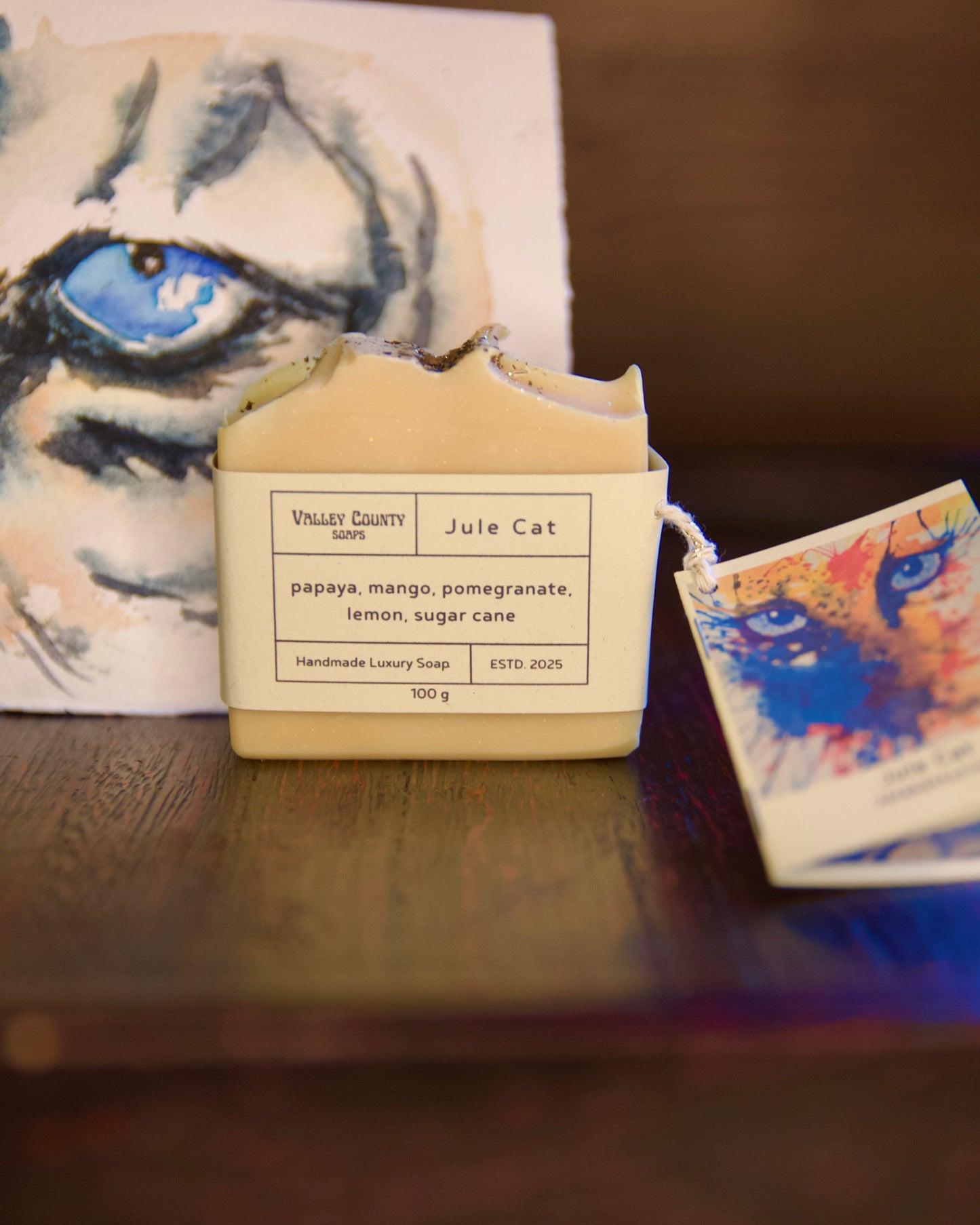 Handmade luxury soap with a label on a wooden surface, featuring a cat illustration in the background.