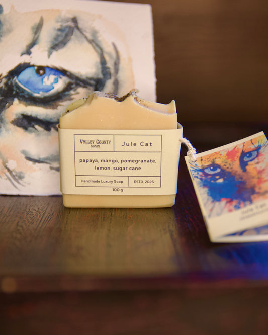 Handmade luxury soap with a label on a wooden surface, featuring a cat illustration in the background.